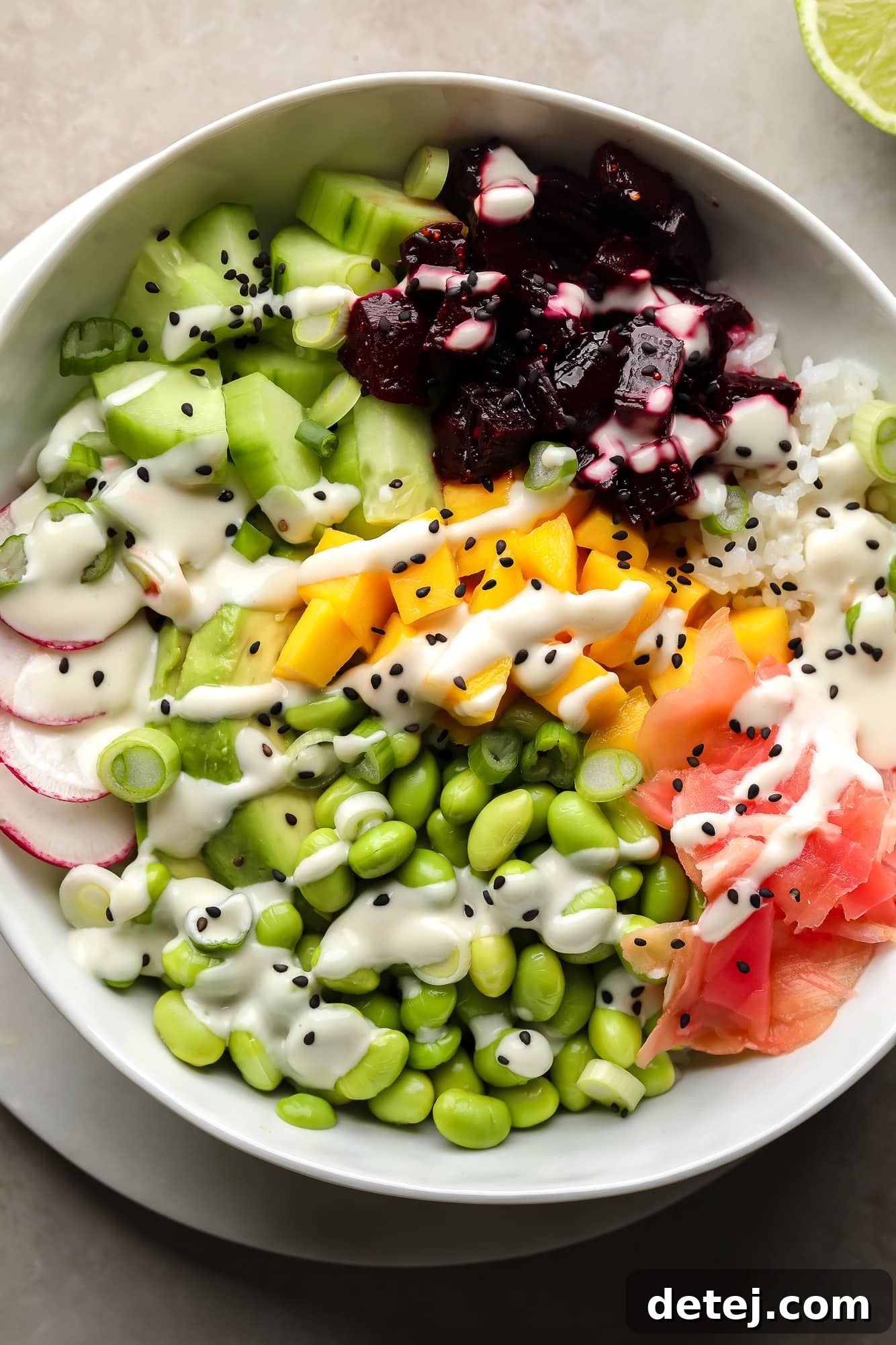 A beautifully assembled vegan beet poke bowl, garnished with marinated beets, sliced mango, colorful radishes, green edamame, fresh cucumber, pickled ginger, and a creamy wasabi mayo drizzle.