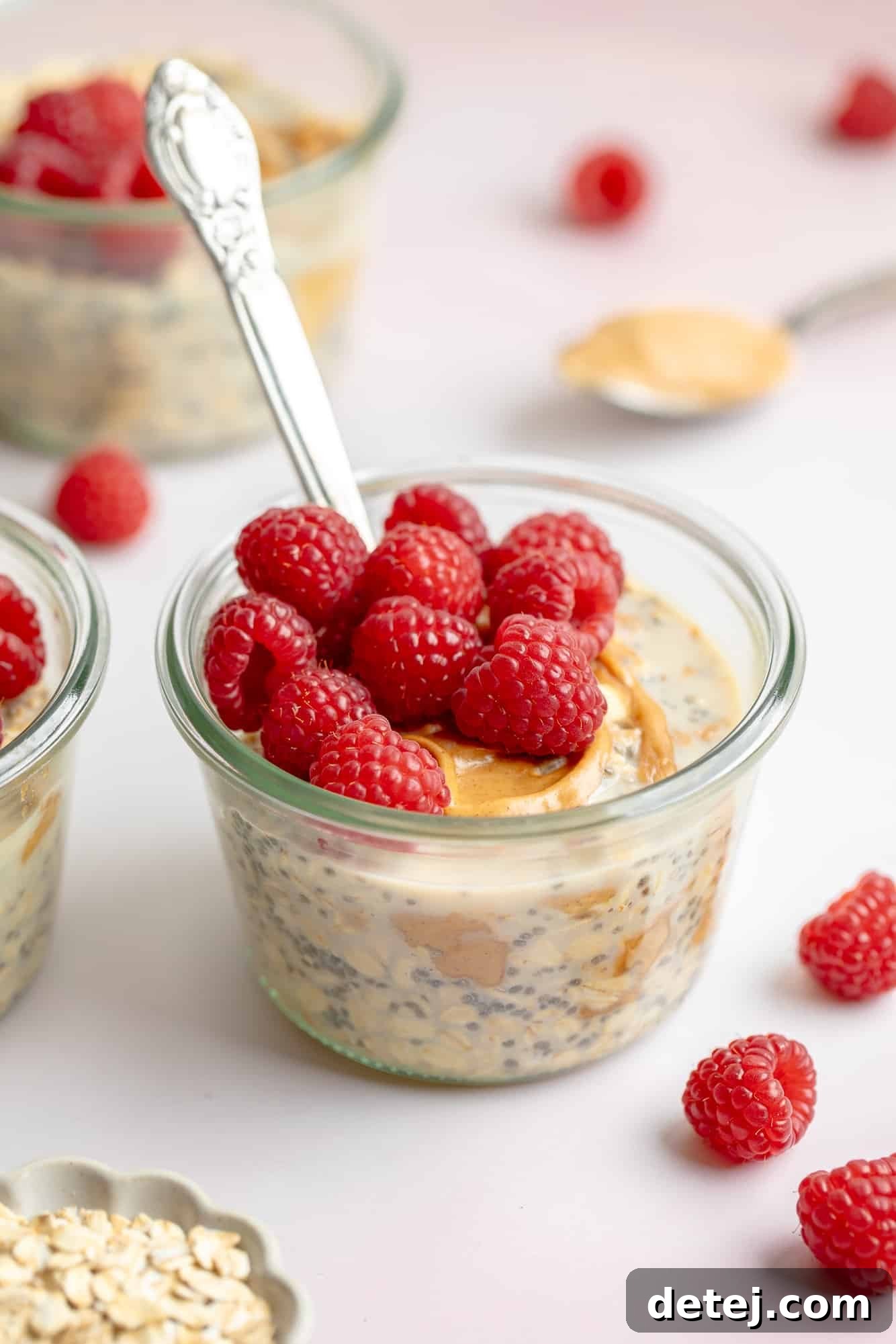 Close up on a jar of creamy peanut butter overnight oats topped with fresh, vibrant raspberries, showcasing the rich texture and appealing presentation of this healthy breakfast.