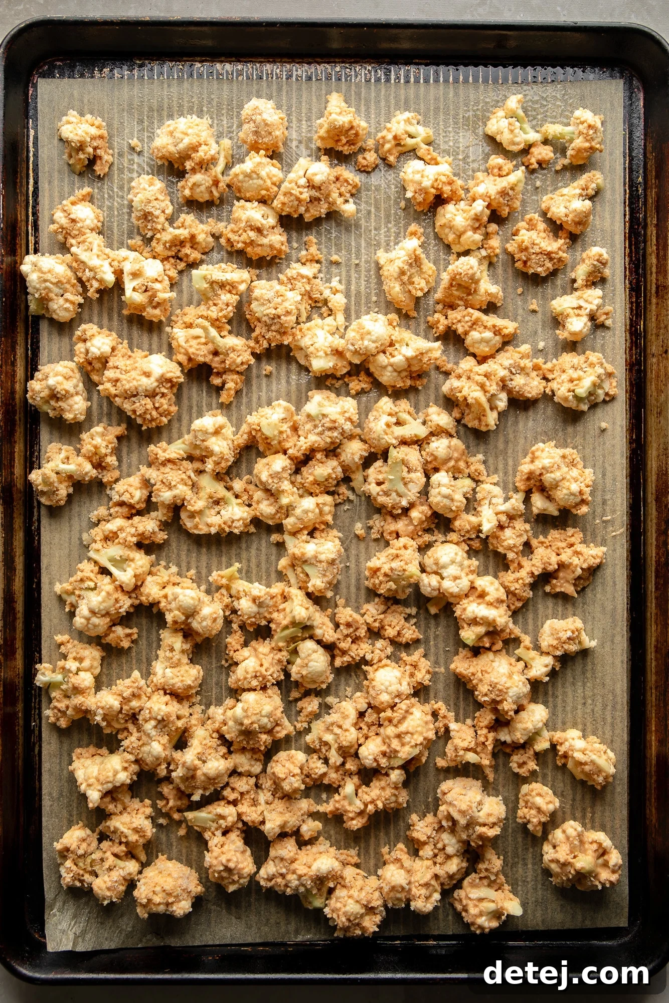 Perfectly breaded cauliflower florets spread evenly on a baking sheet, ready for roasting.