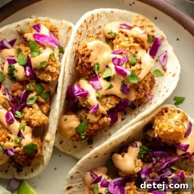 A close-up of three crispy cauliflower tacos on a plate, adorned with fresh toppings.
