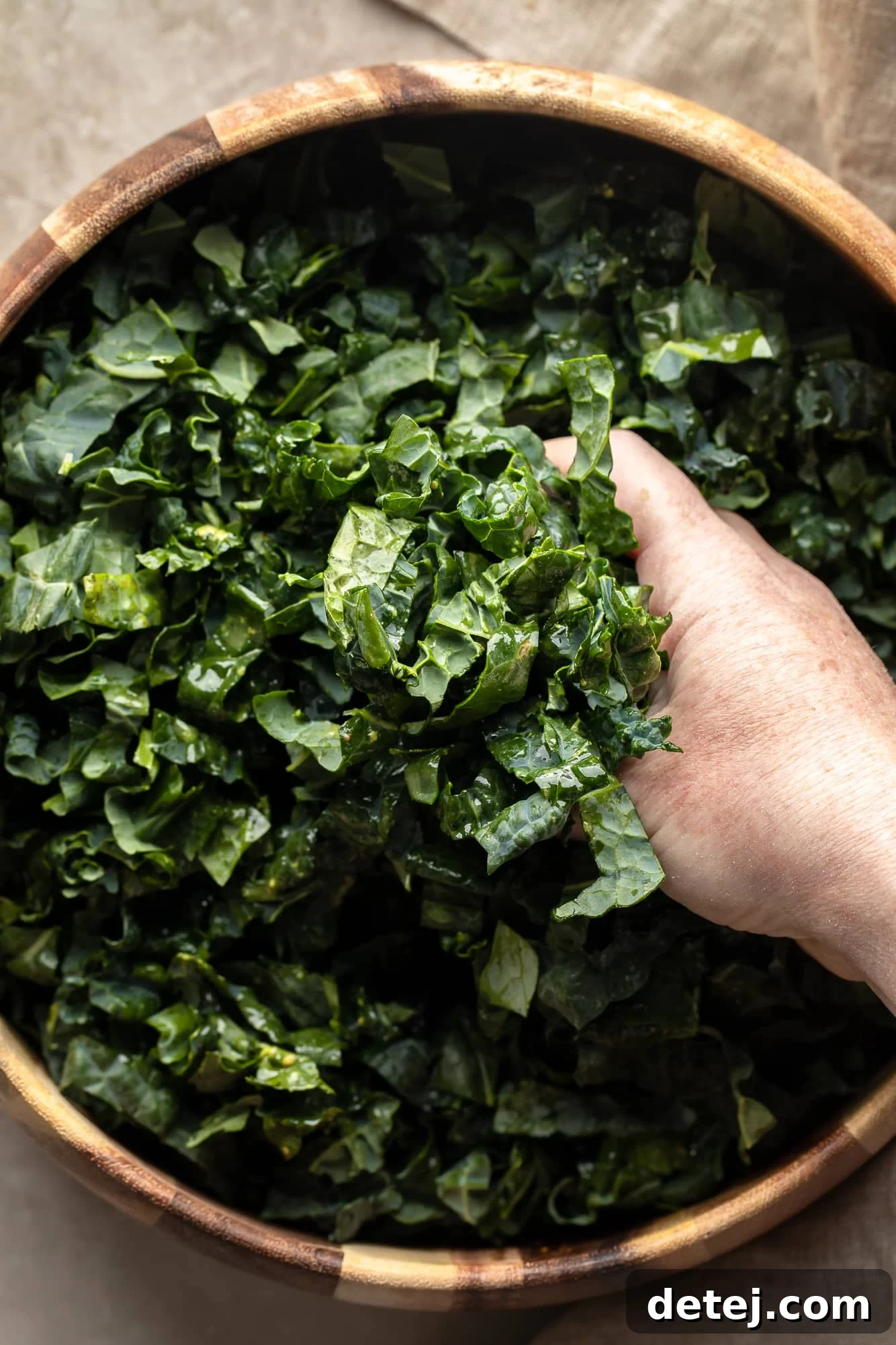 A person's hands gently massaging the kale leaves with dressing in a large salad bowl, softening them to perfection.