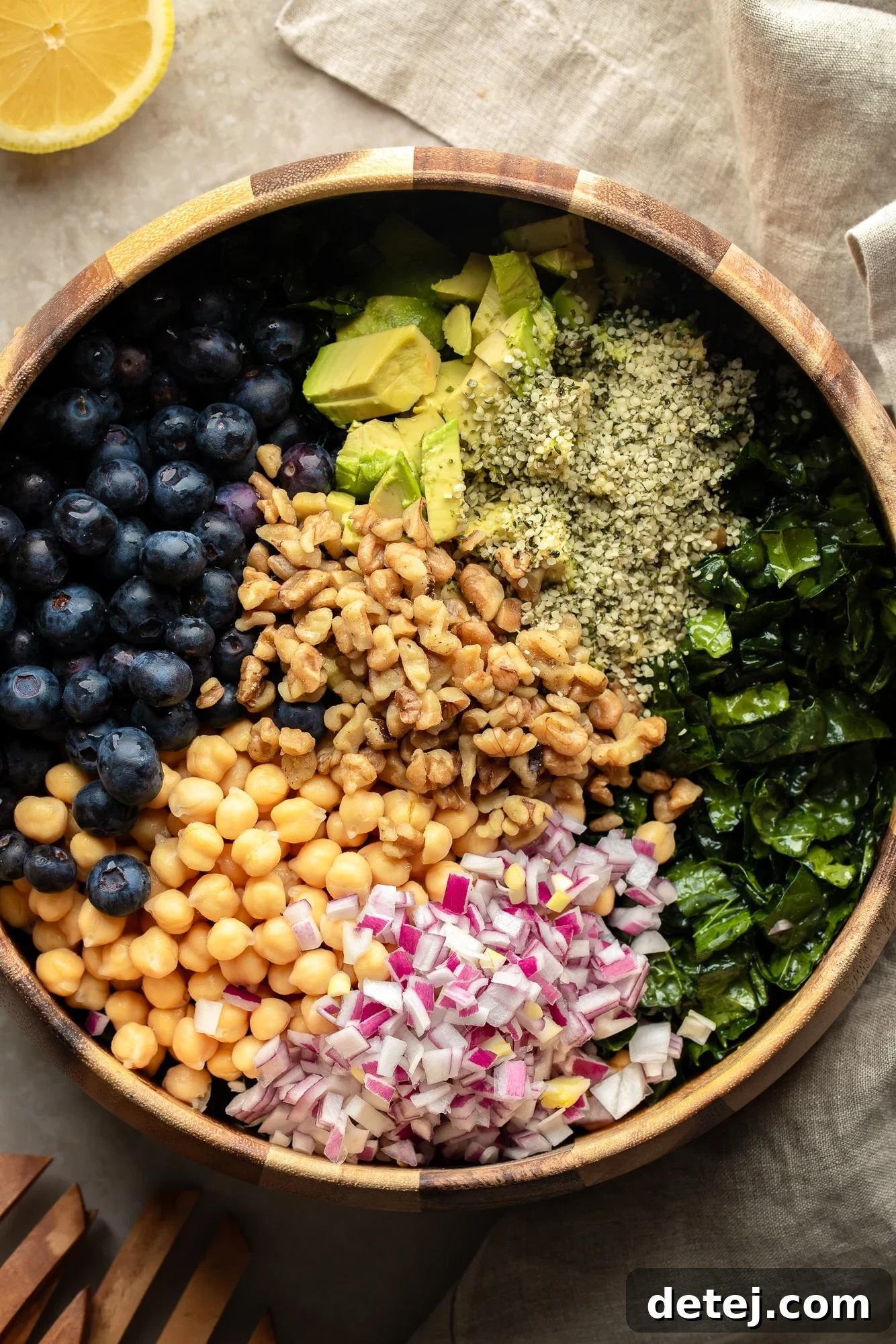 A generously sized kale salad, brimming with a colorful assortment of seeds, nuts, beans, chopped vegetables, and fresh fruits, all perfectly mixed in a large serving bowl.