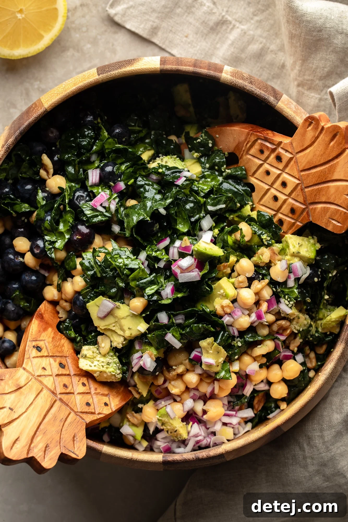 A pair of tongs gently tossing a vibrant kale salad in a large bowl, ensuring all ingredients are well combined and coated with dressing.