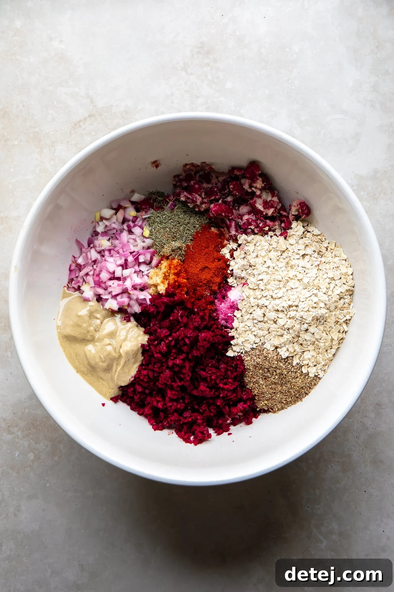 Ruby Red Bean Burgers 4 All the dry and wet ingredients for Kidney Beet Burgers, including mashed kidney beans, shredded beets, diced red onion, garlic, and spices, mixed together in a large white bowl, vibrant and ready for patty formation.
