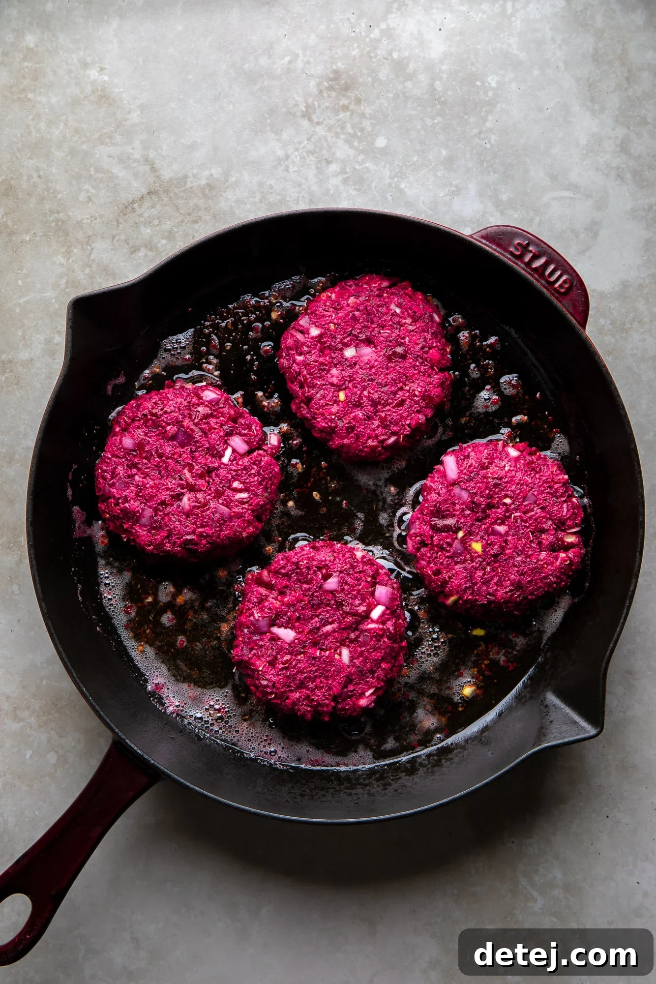 Ruby Red Bean Burgers 5 Four vibrant kidney beet burgers sizzling and frying in a cast iron pan, turning golden brown and developing a crispy exterior.