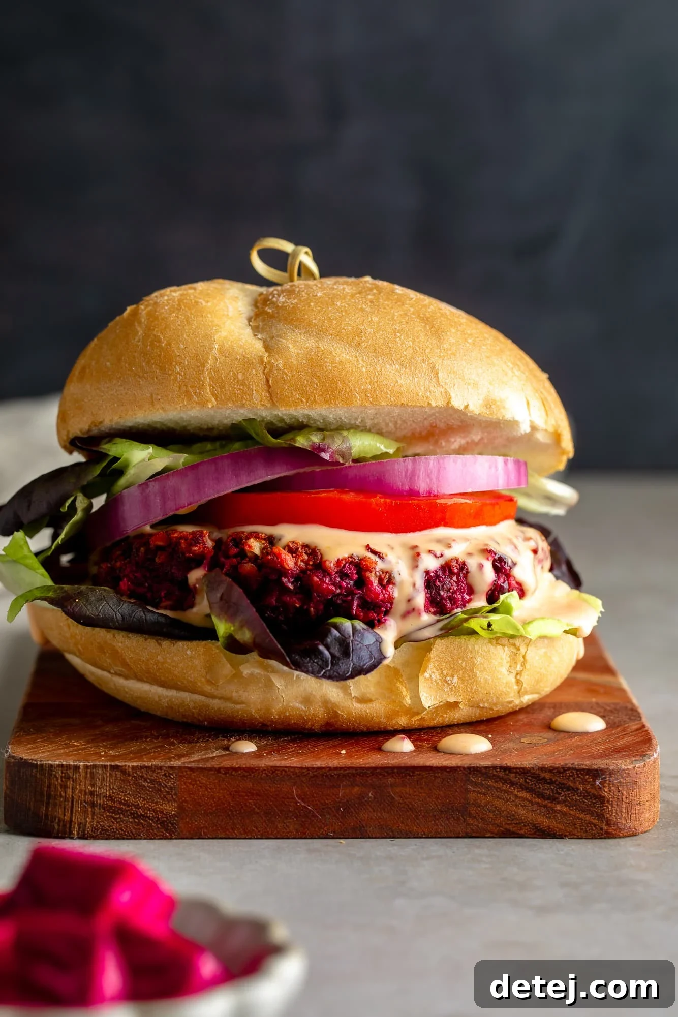 Ruby Red Bean Burgers 6 A close-up shot of a perfectly assembled Kidney Beet Burger on a toasted bun, loaded with crisp lettuce, juicy tomato, red onion slices, and a generous drizzle of creamy sriracha mayo, showcasing its vibrant layers and inviting texture.