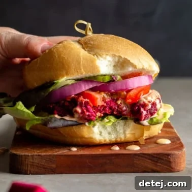 Ruby Red Bean Burgers 7 A woman's hand holding a vibrant kidney beet burger with a bite taken out of it, showcasing its tender, meaty interior and beautiful red color. Garnished with fresh toppings.