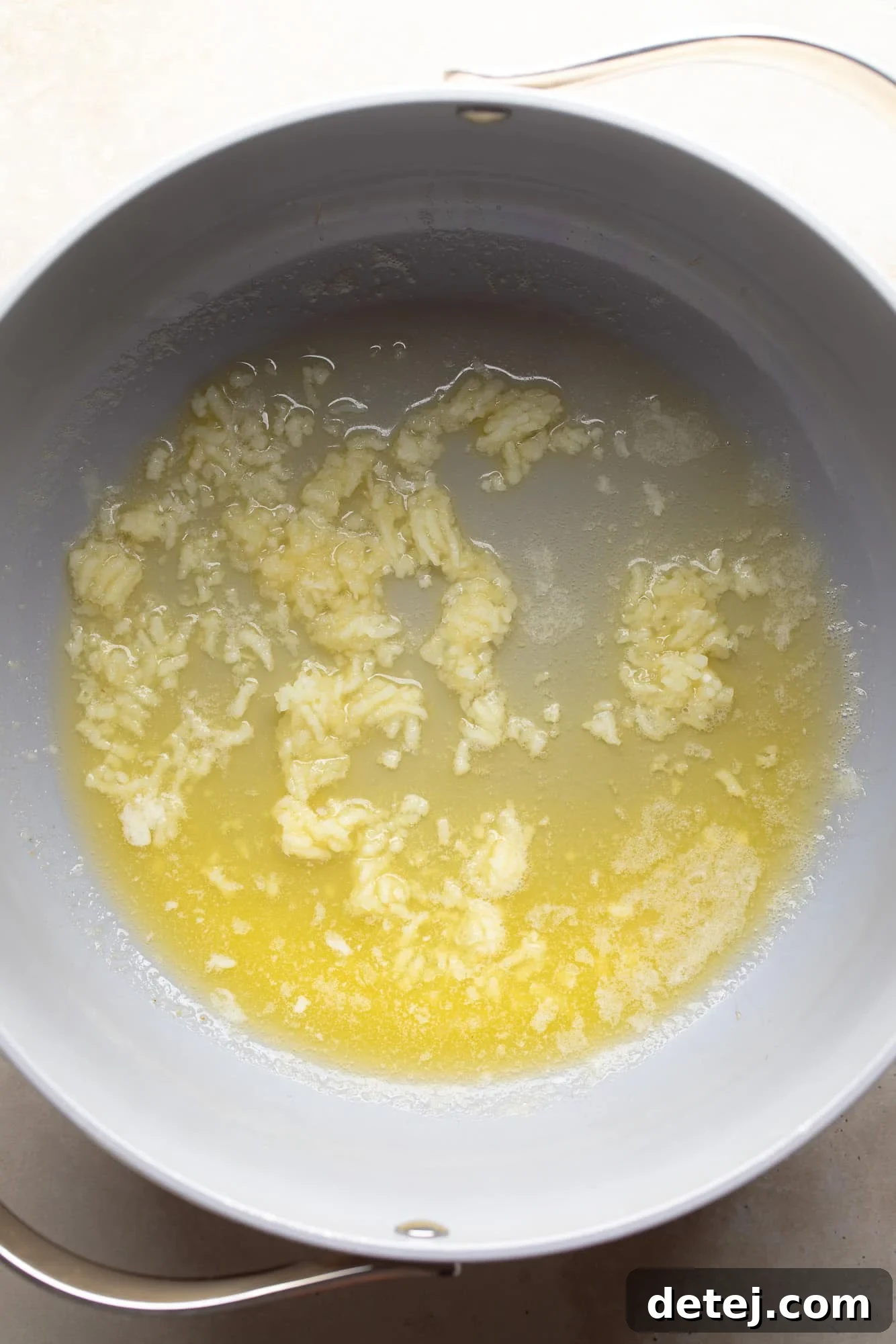 Freshly minced garlic sautéing in melted vegan butter in a grey non-stick skillet.