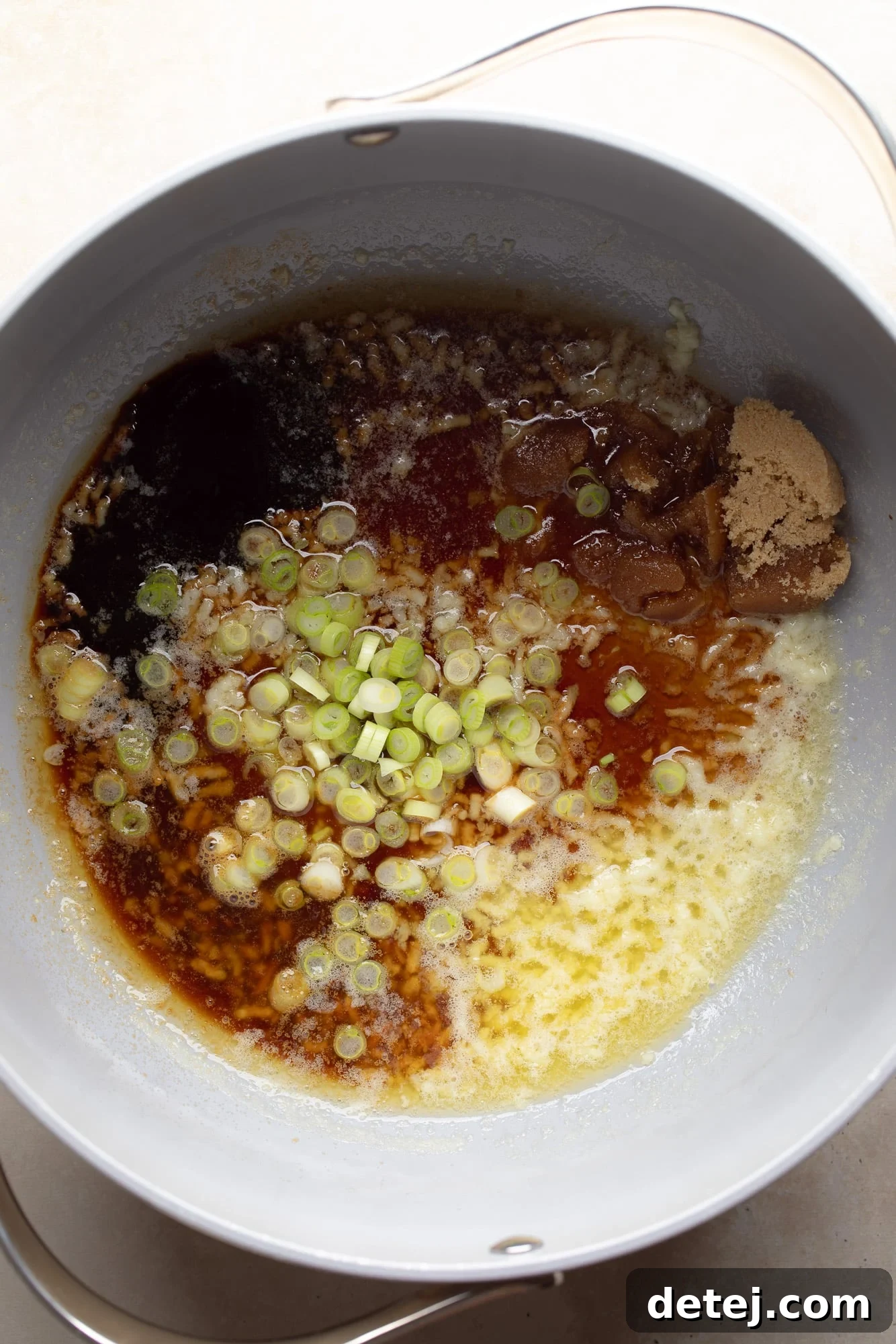 Ingredients for the garlic sauce, including soy sauce, oyster sauce, sesame oil, brown sugar, and green onions, gathered in a grey skillet.