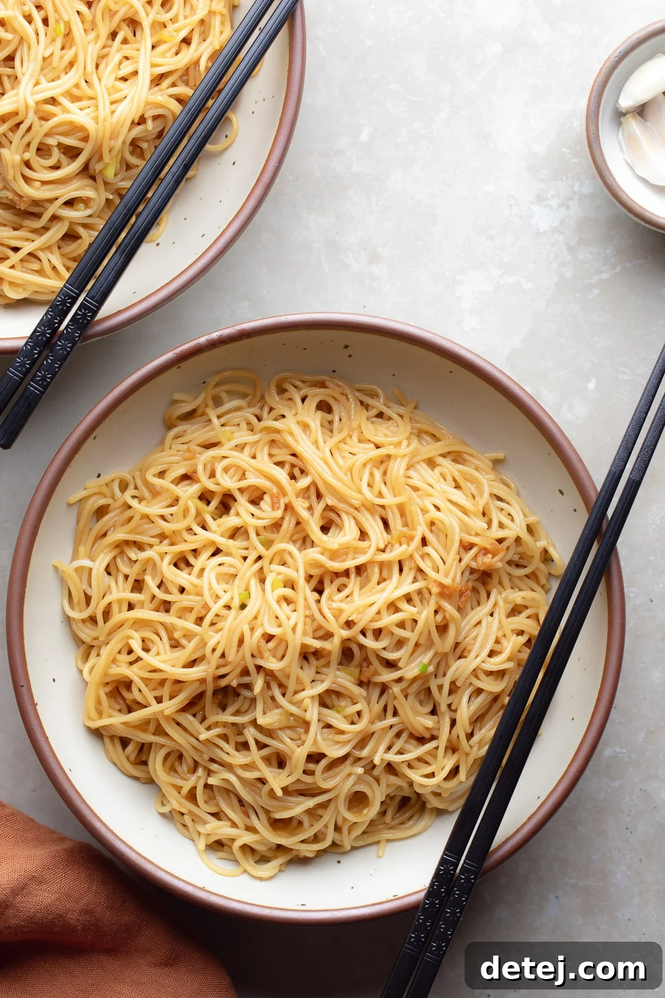 A beautifully plated bowl of garlic noodles, adorned with fresh green onions and black chopsticks resting on the side.