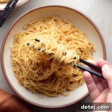 A hand using chopsticks to lift garlic noodles up from a bowl, showcasing their deliciousness.
