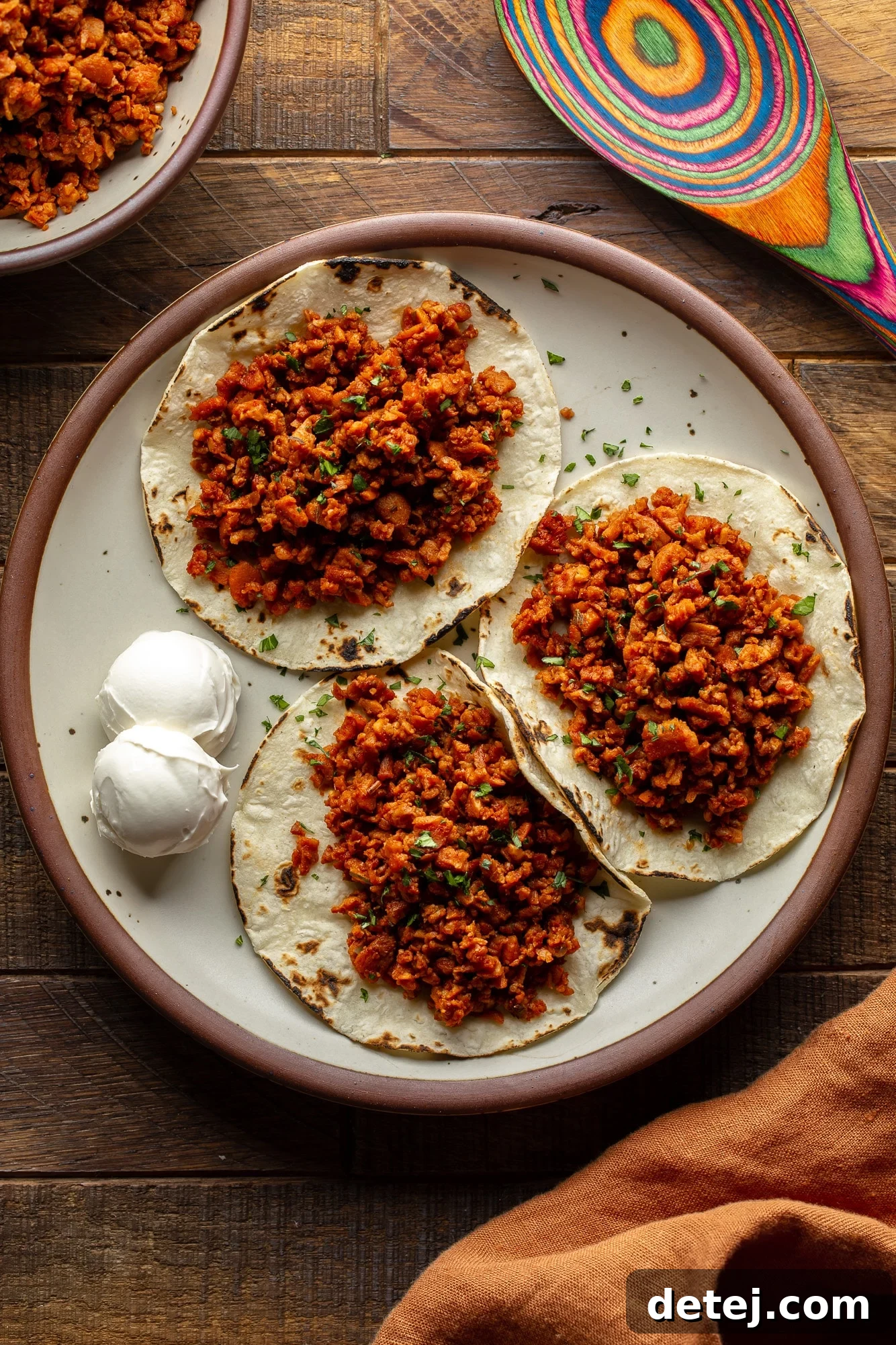 Plant-Based Chorizo 2 three tortillas topped with vibrant vegan chorizo crumbles on a rustic plate, garnished with fresh cilantro and lime wedges.
