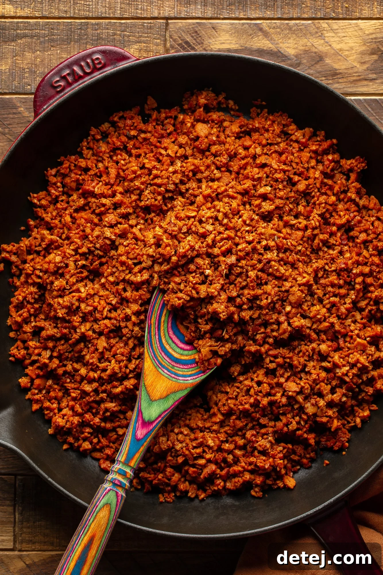 Plant-Based Chorizo 3 A wooden spoon actively stirring a batch of vegan chorizo crumbles in a large non-stick skillet over medium heat.