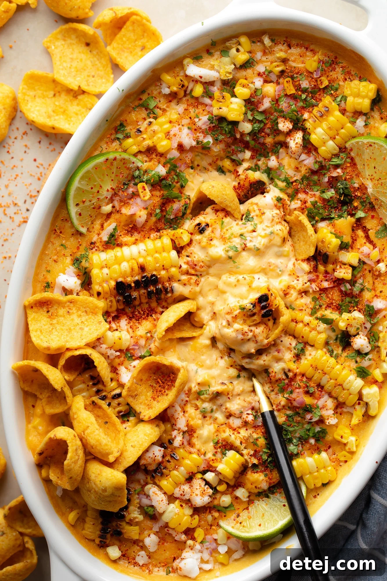 A black spoon serving a portion of vibrant dairy-free Mexican Street Corn Dip from a baking dish, showcasing charred corn kernels and a creamy texture.
