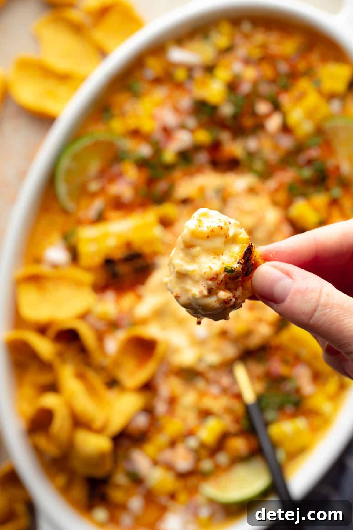 A hand holds a corn chip, laden with a generous scoop of the creamy, vibrant Vegan Mexican Street Corn Dip, ready to be enjoyed.