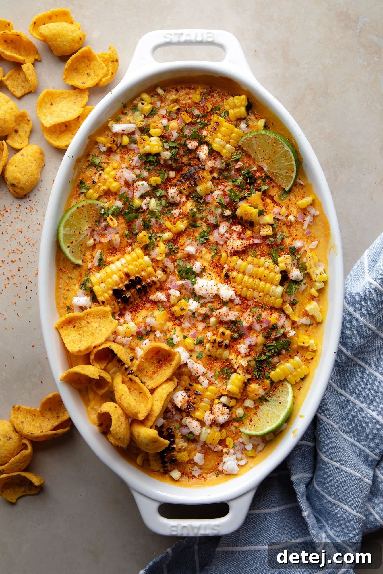 The finished vegan Mexican Street Corn Dip, garnished with charred corn, fresh cilantro, and lime wedges, served with a side of corn chips in a baking dish.