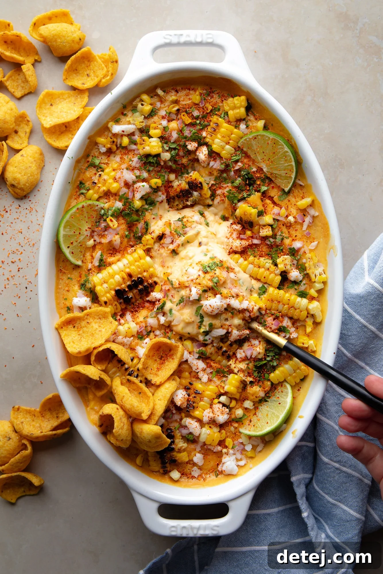 A black spoon sits in a baking dish full of rich, creamy vegan Mexican Street Corn Dip, topped with vibrant cilantro and charred corn.
