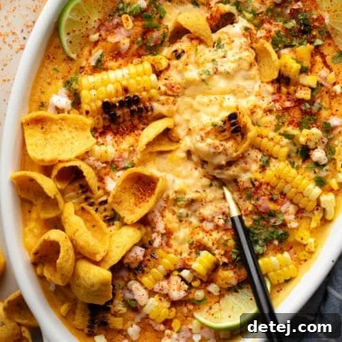 Close-up of a black spoon in a baking dish of vegan Mexican Street Corn Dip, showing off its creamy texture and charred corn.