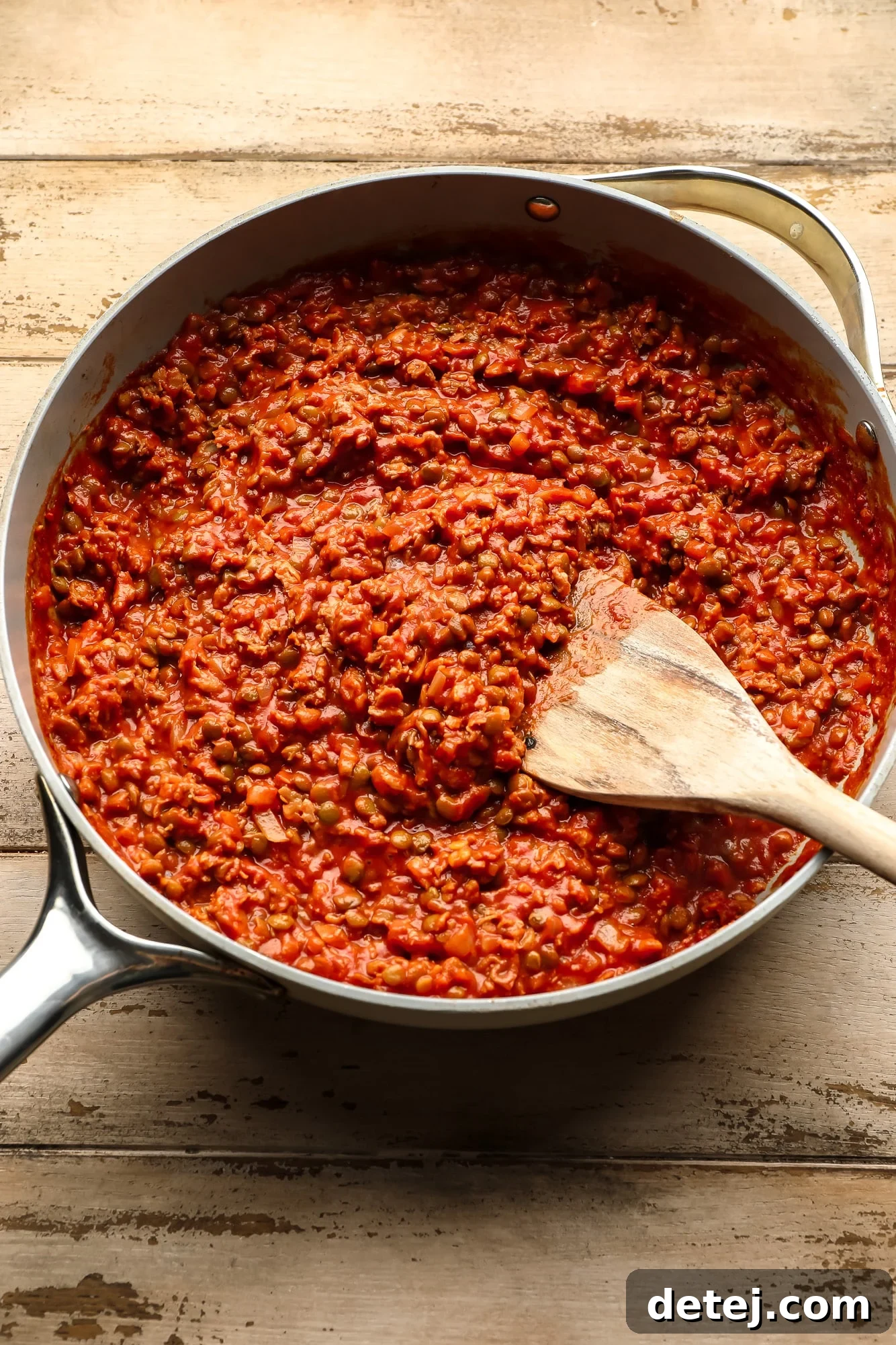 stirring a vegan sloppy joe mixture with a wooden spoon in a skillet.