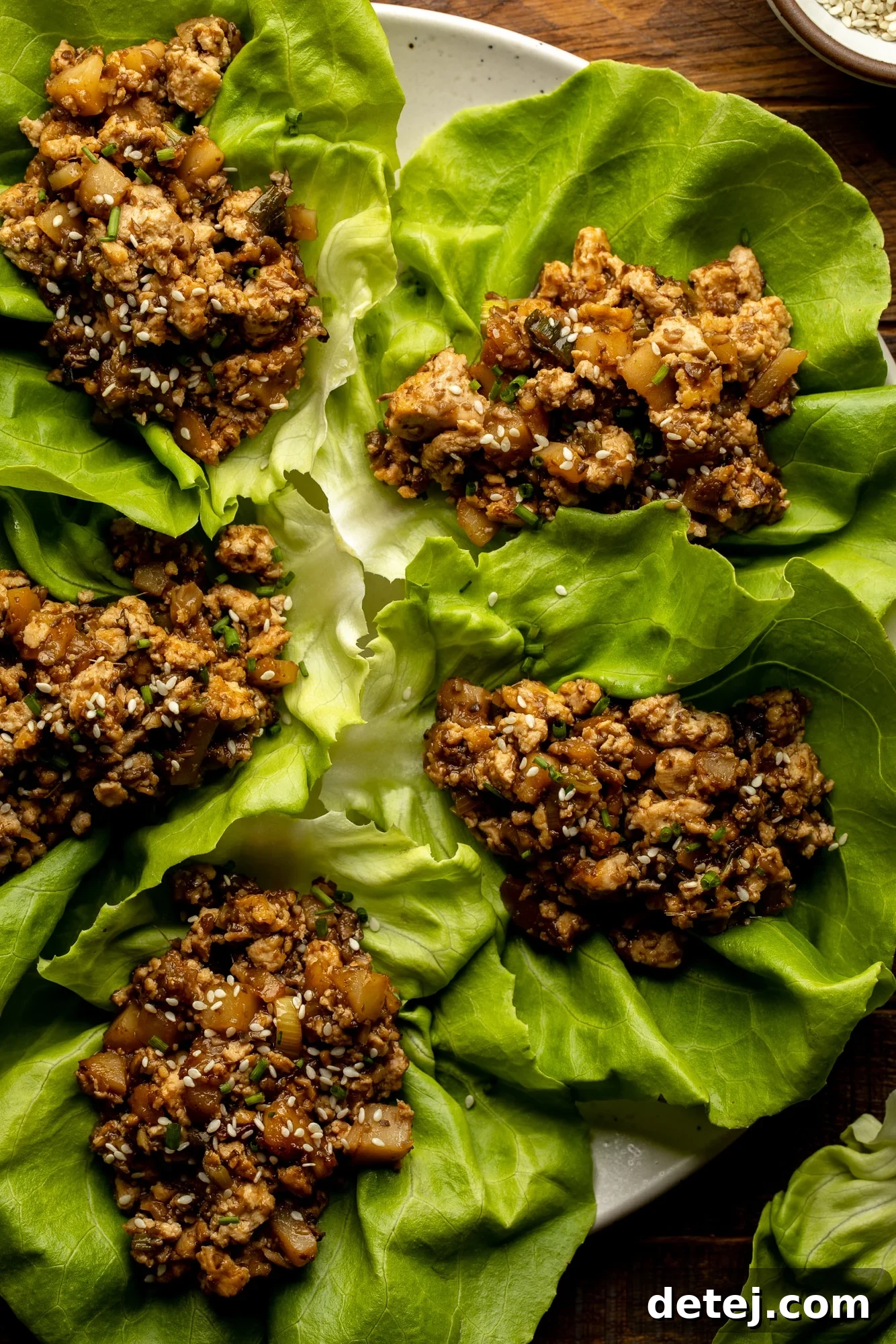 Overhead view of a vibrant plate of Tofu Lettuce Wraps, featuring crisp lettuce cups overflowing with a rich, savory tofu filling, garnished with fresh green onions and a drizzle of sauce, inviting diners to enjoy a healthy and flavorful meal.