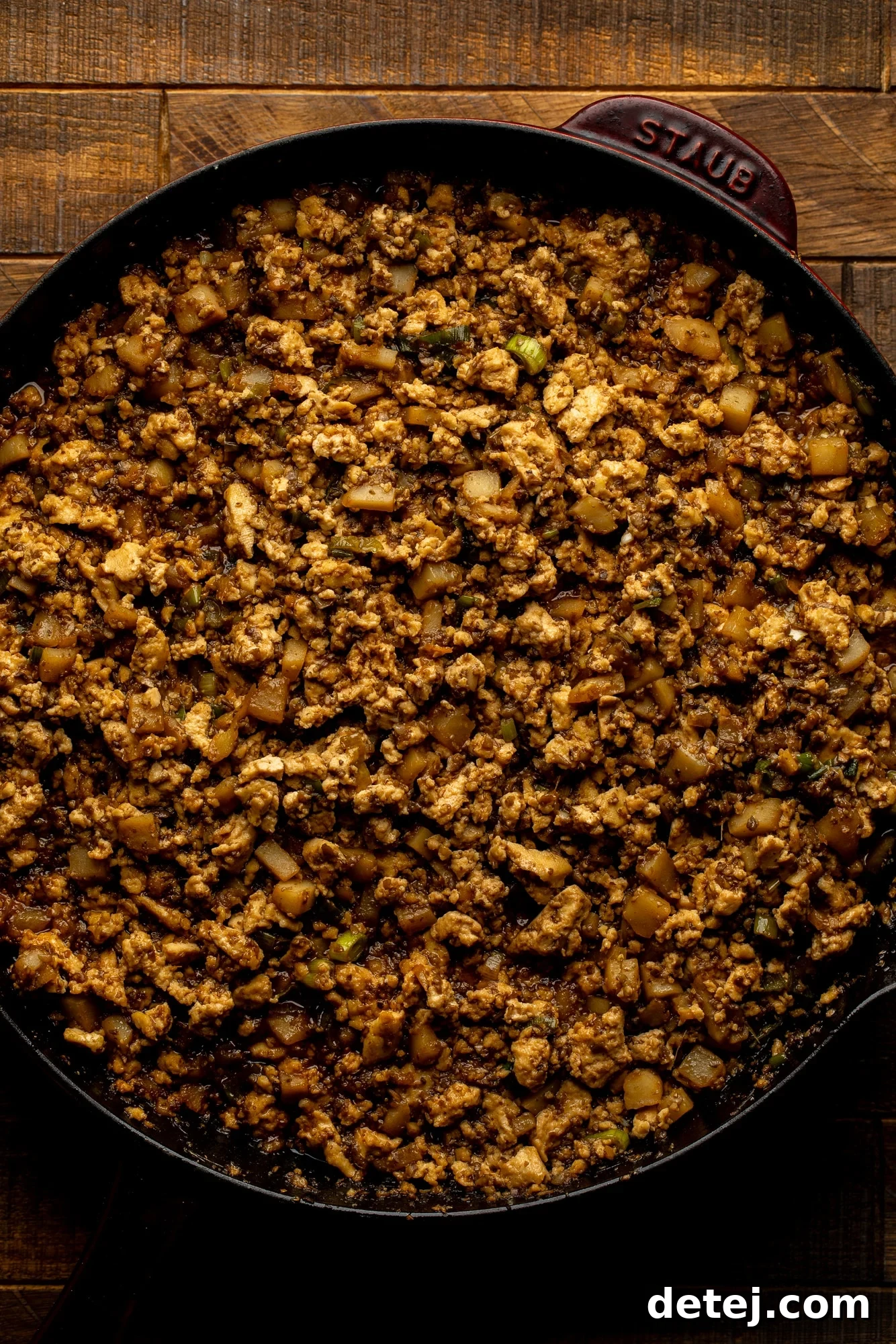 Close-up view of the savory tofu filling being cooked in a large black skillet, with mushrooms, water chestnuts, and green onions visible, all coated in a rich, dark sauce, ready to be scooped into lettuce wraps.