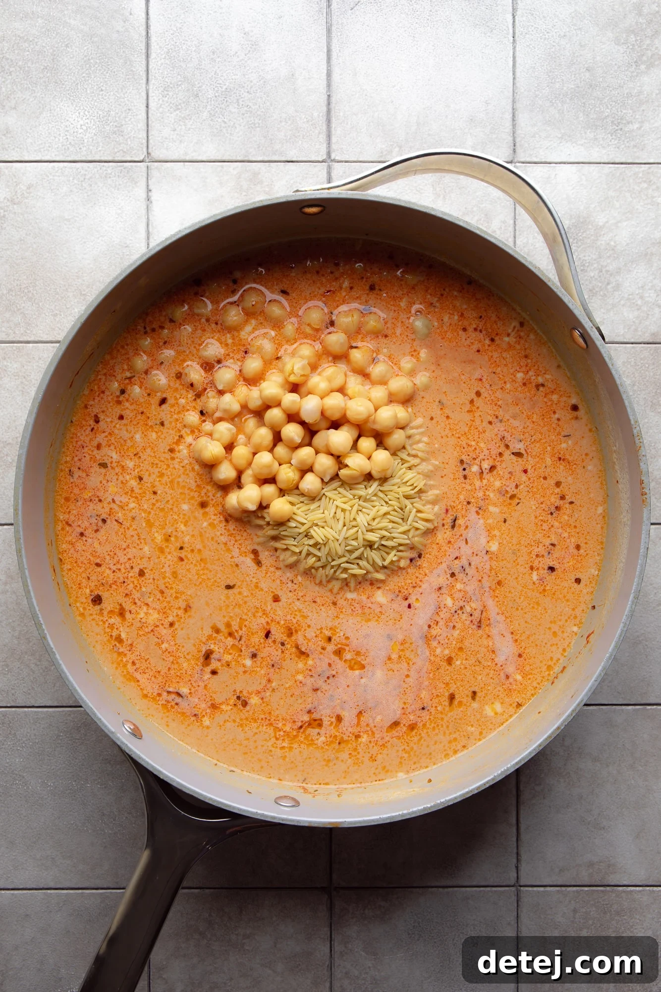 Chickpeas and orzo pasta simmering in a rich orange tomato sauce in a skillet, showing the consistency.