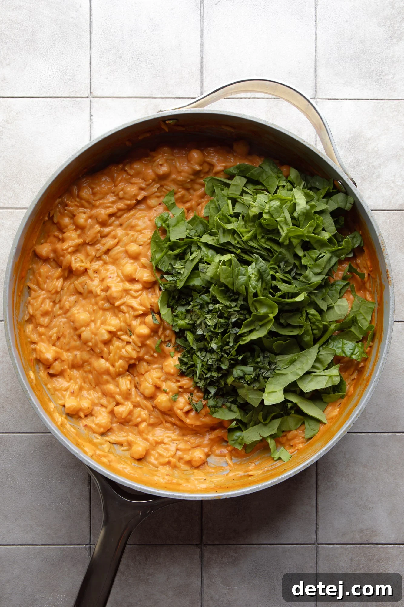 Chopped fresh spinach being added to the creamy tomato orzo in a skillet, ready to be stirred in.