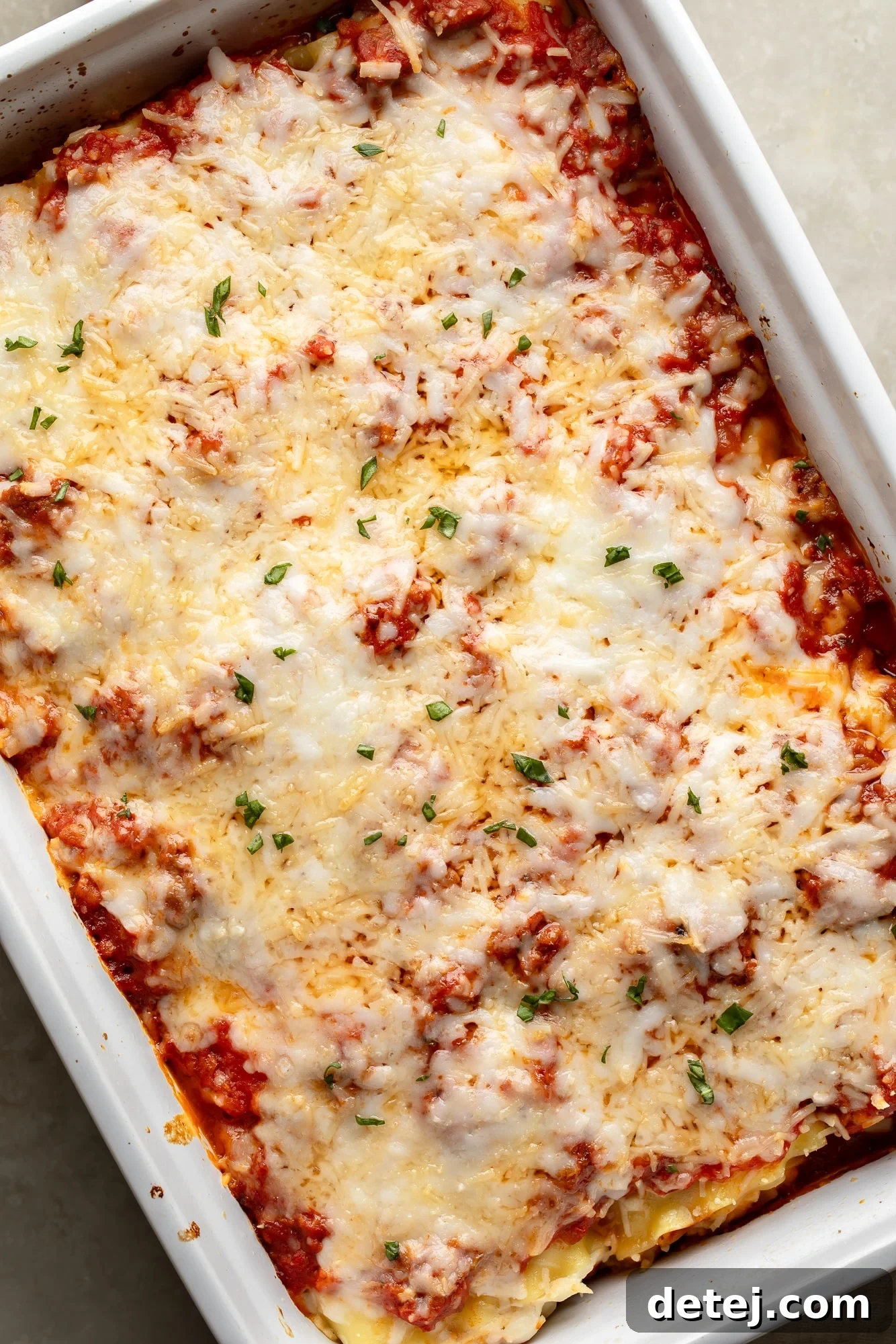 Overhead view of a white casserole dish filled with unbaked vegan lasagna rolls, generously covered with cheese and marinara sauce, ready for the oven.