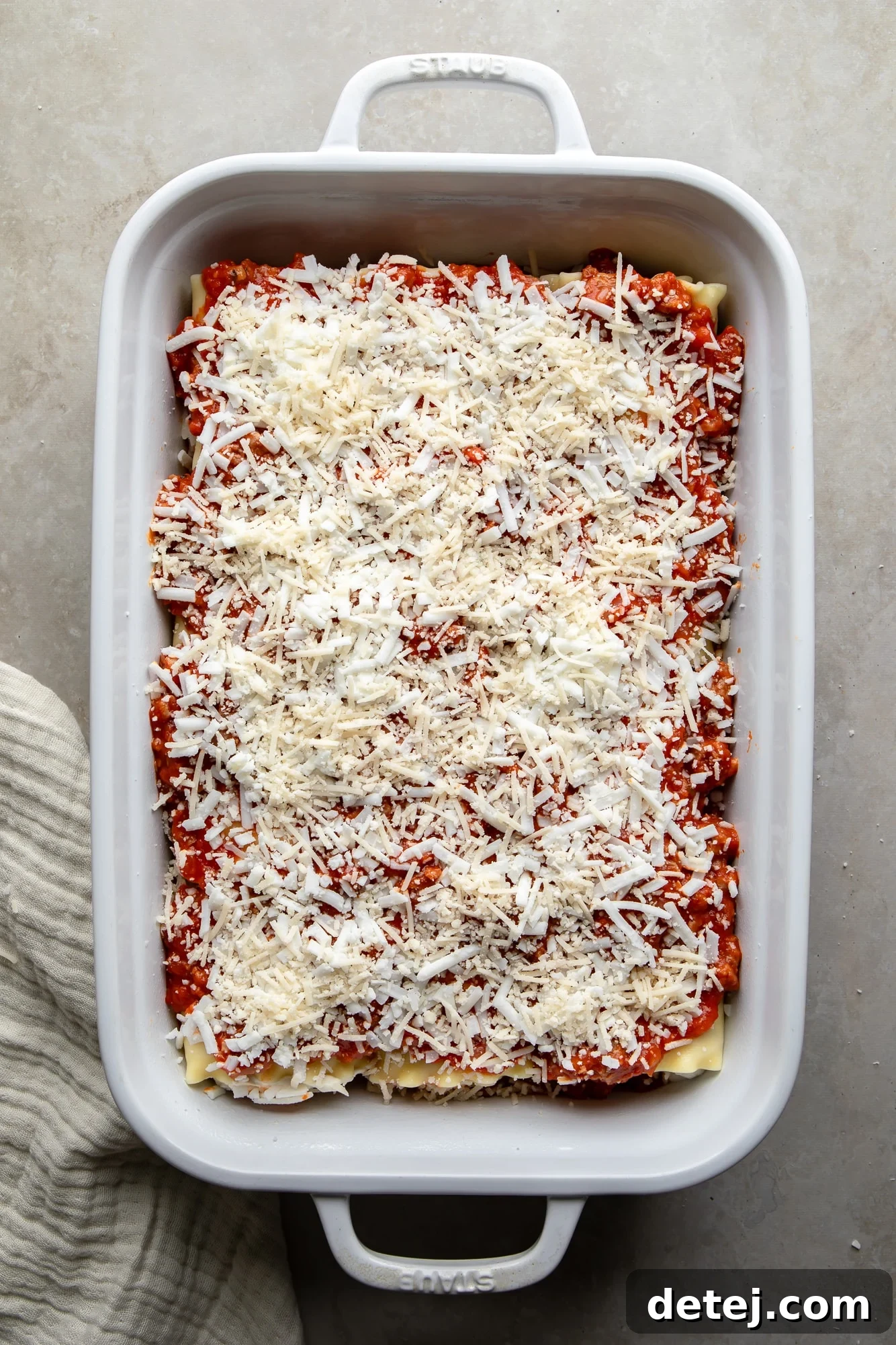 Overhead view of unbaked, cheese-covered vegan lasagna rolls resting in a white casserole dish, awaiting their turn in the oven.