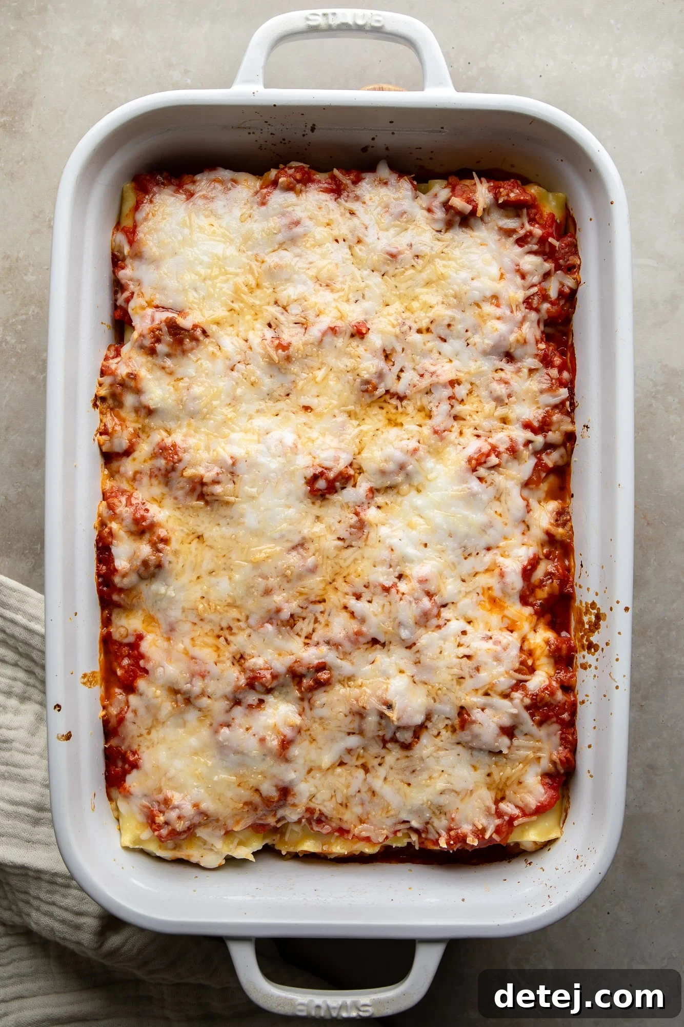 Overhead view of golden-brown, cheese-covered vegan lasagna rolls bubbling in a white casserole dish, fresh out of the oven.