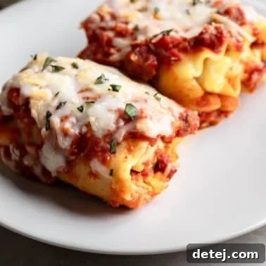 close up on two baked vegan lasagna rolls on a white plate.
