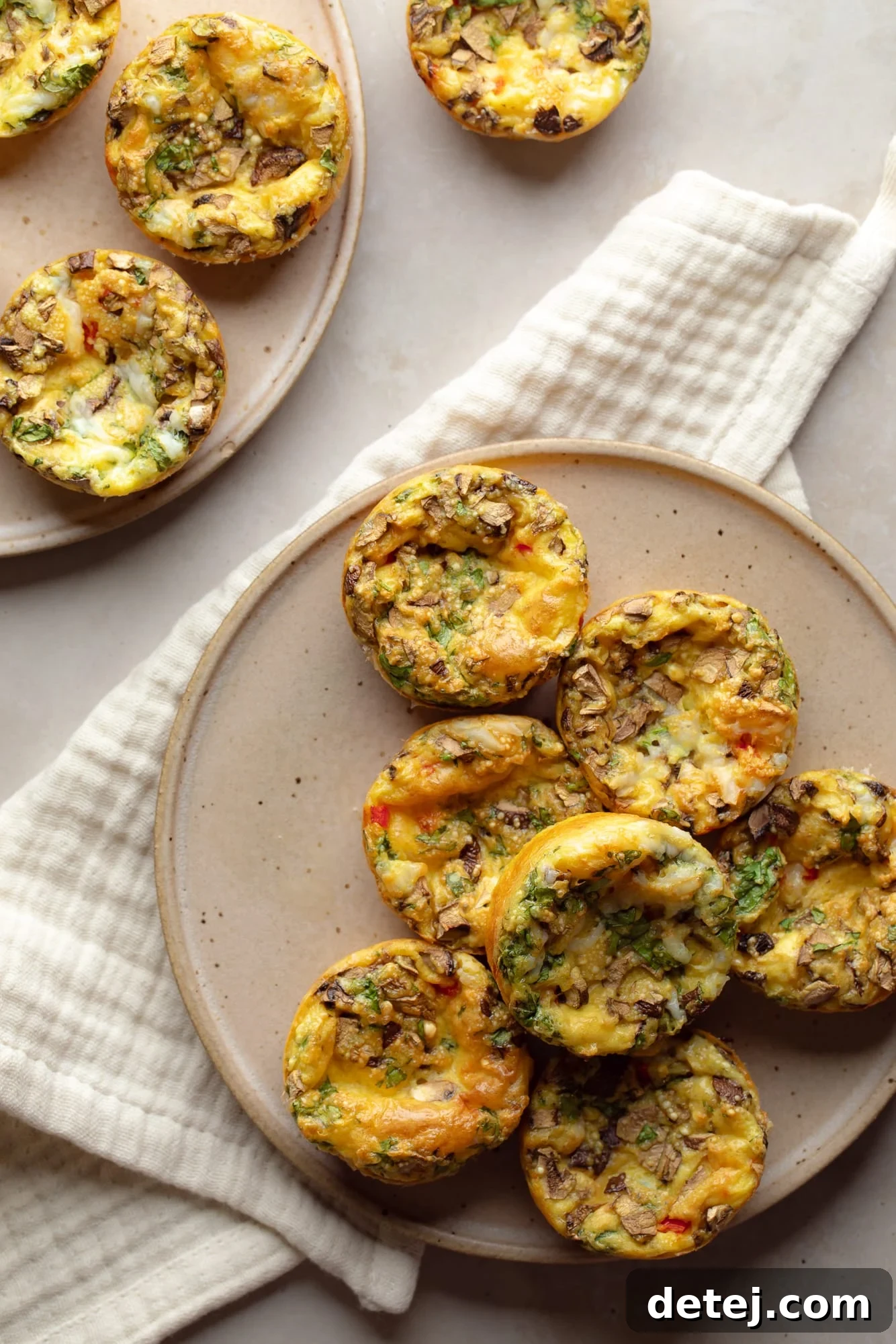 Overhead view of a stack of fluffy vegan egg muffins on a white plate, garnished with fresh herbs, showcasing their golden-brown tops and vibrant veggie fillings. Perfect for a quick and healthy breakfast or snack.