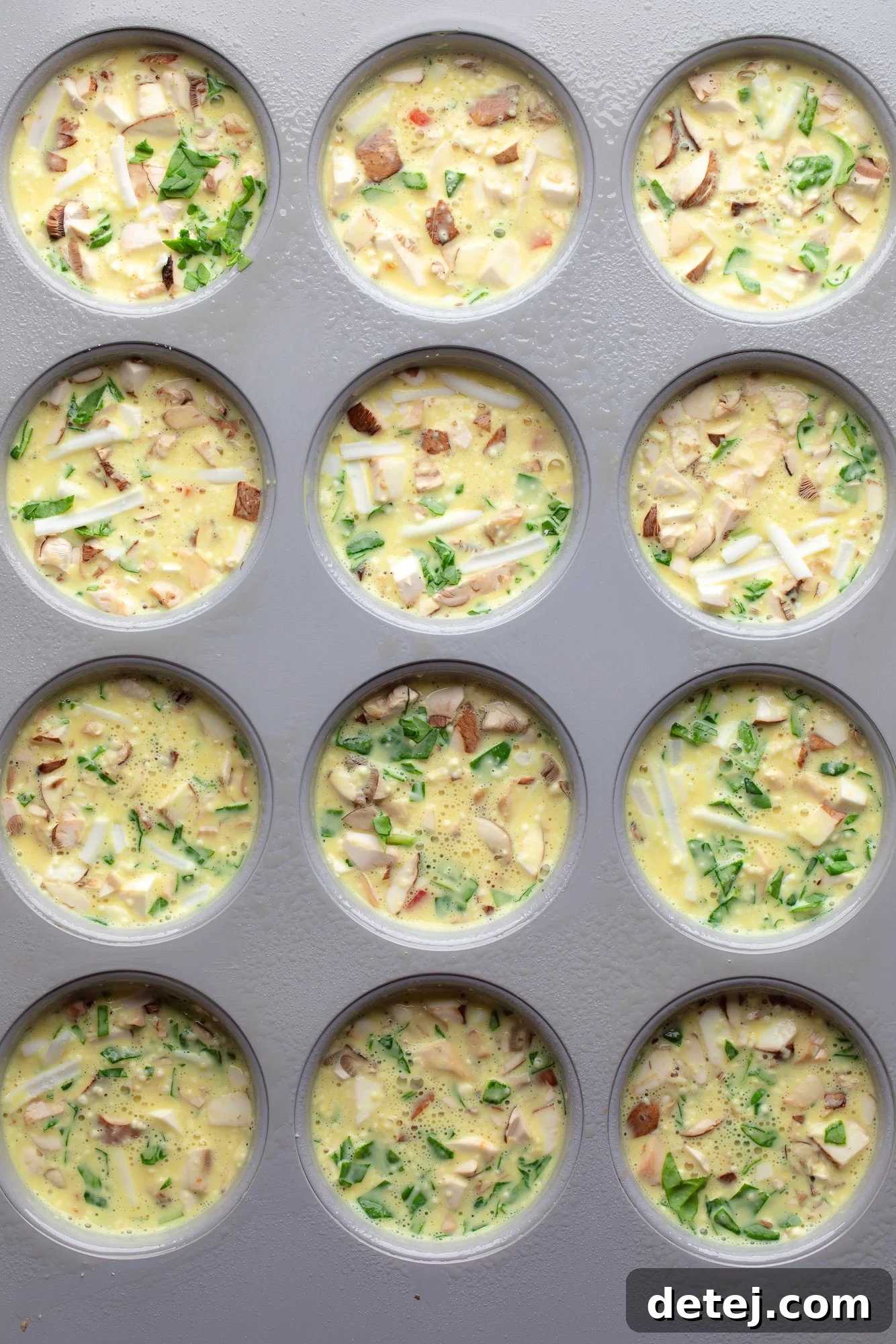 Uncooked vegan egg muffins in a muffin tin, with the liquid JUST Egg mixture poured over the vegetables and vegan cheese, before baking.