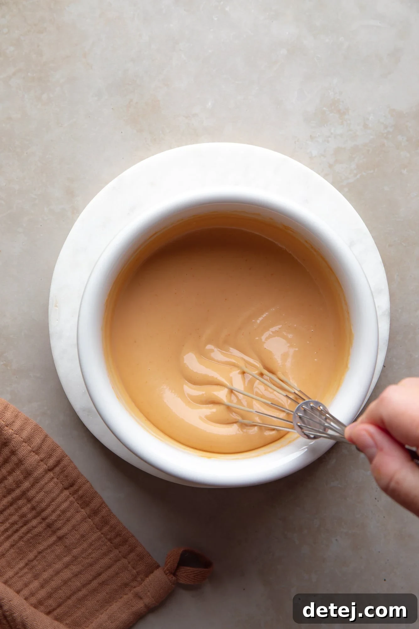 a womans hand whisking a creamy sriracha sauce in a white bowl.