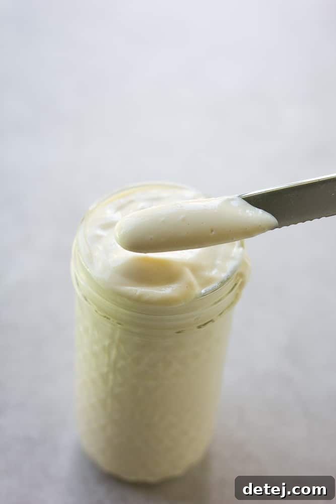 Homemade tofu vegan mayonnaise in a glass jar with a knife spreading it
