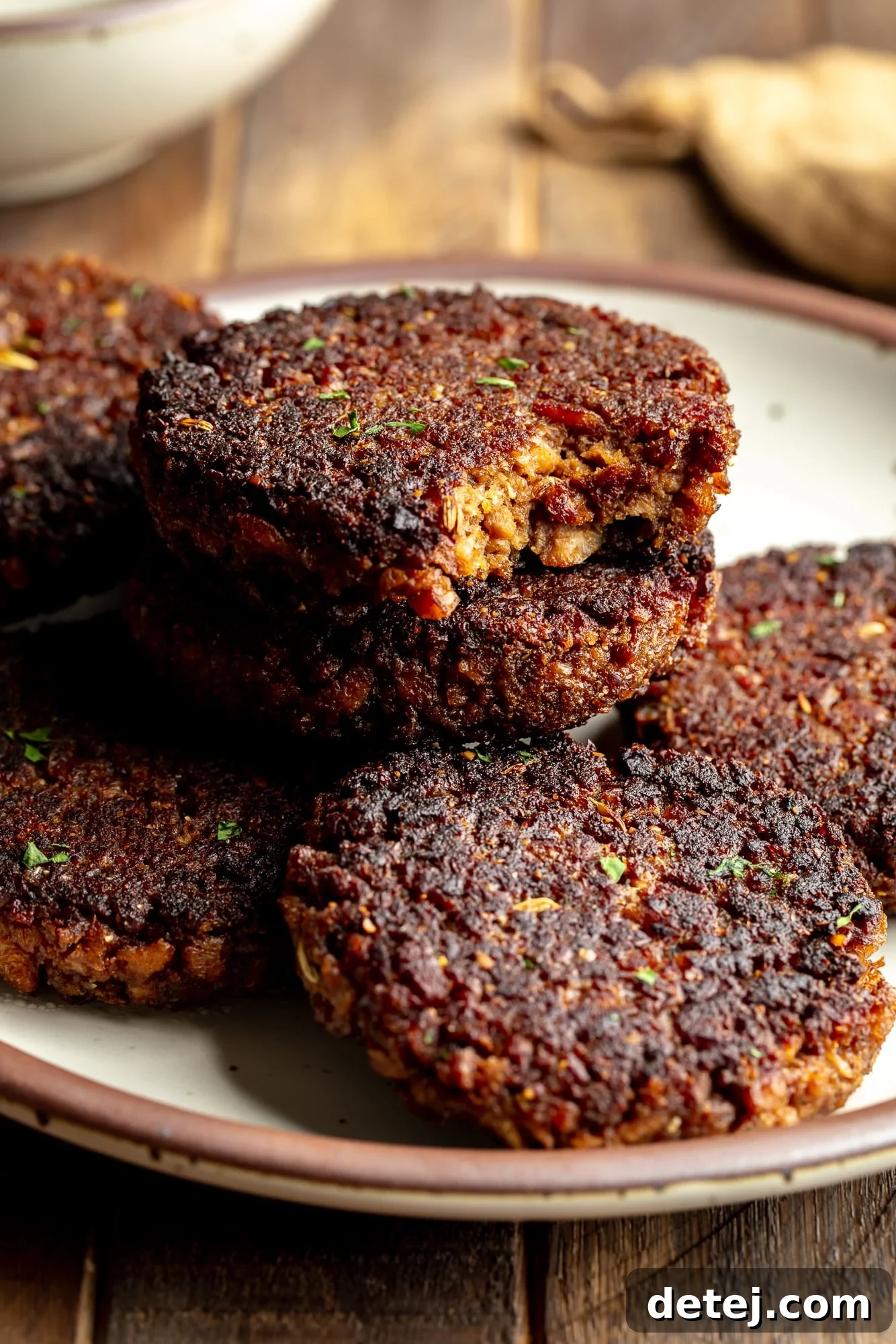 close up on a pile of vegan breakfast sausage patties on a plate, with the top sausage missing a bite.