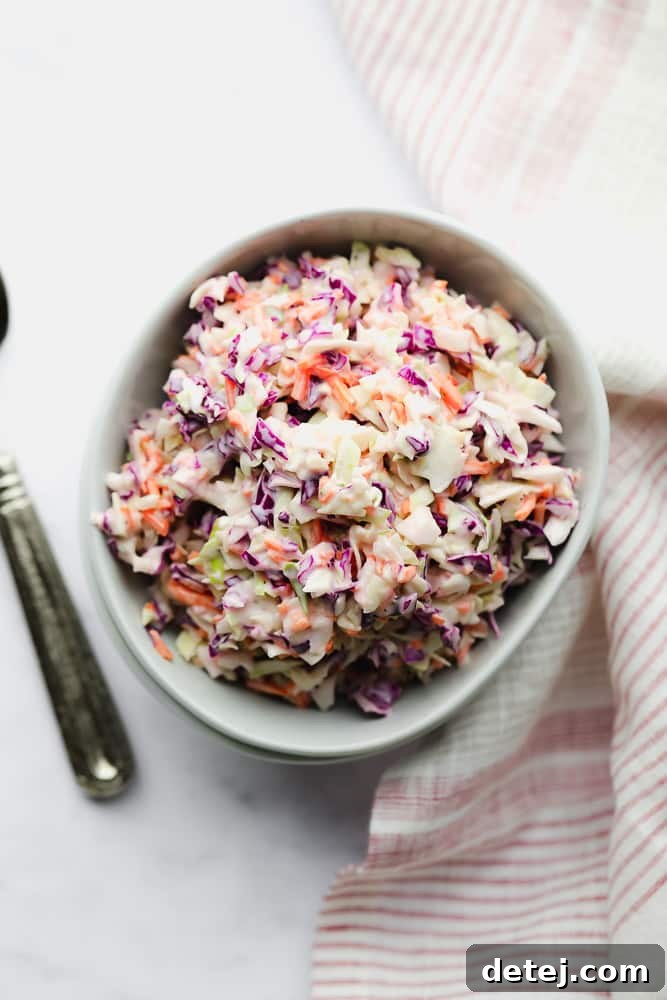 Looking down on a bowl of vibrant vegan coleslaw in white bowls, accented by a red and white striped towel.