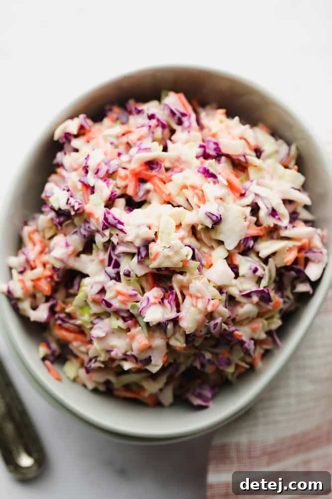 A close-up view of a bowl of vegan coleslaw, perfectly mixed, with a red and white striped towel visible nearby.