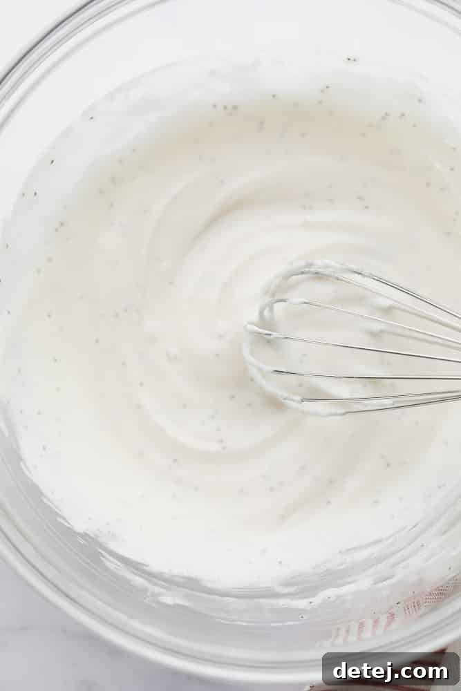 A creamy vegan coleslaw dressing being whisked in a glass bowl.