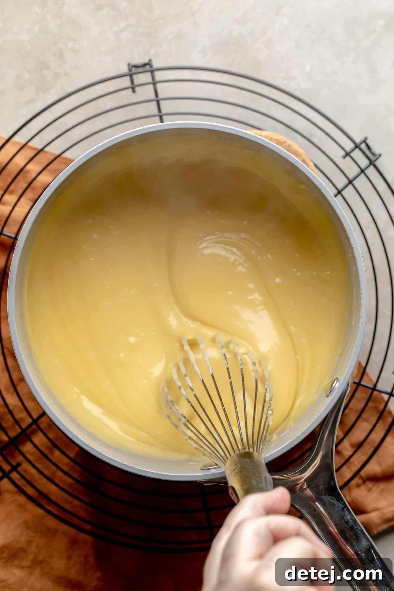 Plant-Based Philly Delight 6 A woman's hand whisking vegan cheese sauce in a saucepan, showing its smooth consistency.