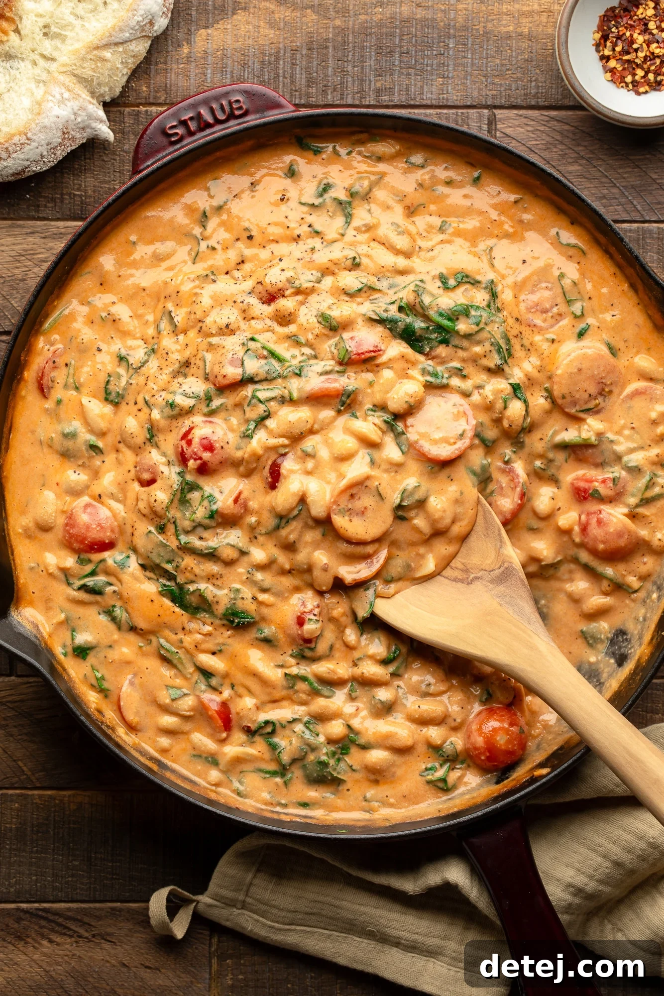 A wooden spoon scooping up creamy skillet white beans from a large pan, showcasing the rich sauce and tender beans.