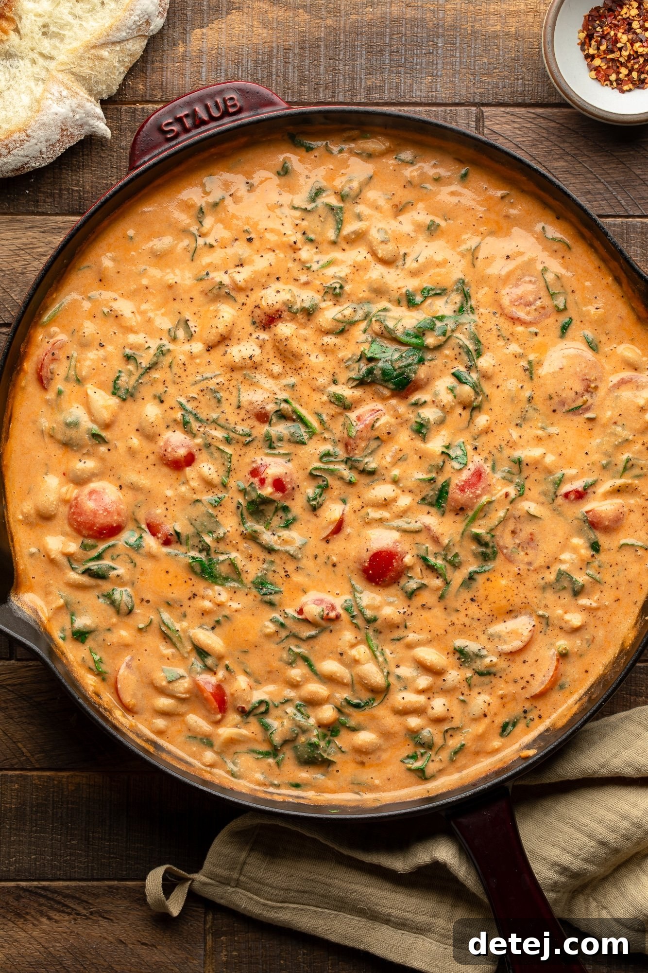 A large skillet brimming with creamy white beans, vibrant spinach, fresh basil, and ripe cherry tomatoes in a rich tomato cream sauce.