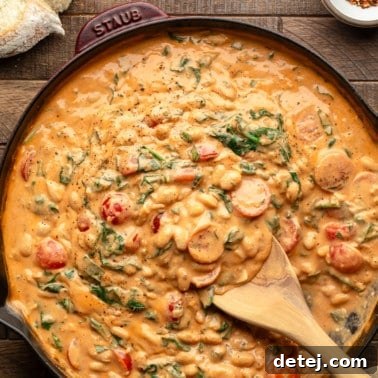 Square image of a wooden spoon scooping up skillet white beans from a large pan, emphasizing the creamy texture.