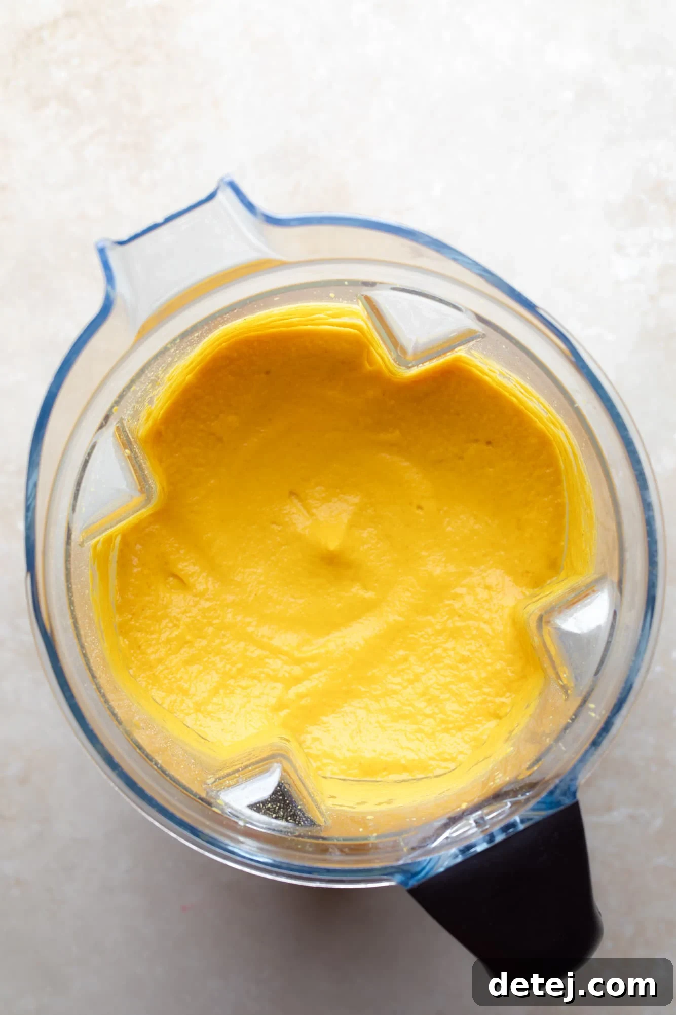 A high-powered blender showcasing a perfectly smooth, vibrant orange vegan pumpkin cheese sauce. The texture is thick and creamy, ready to be tossed with pasta.