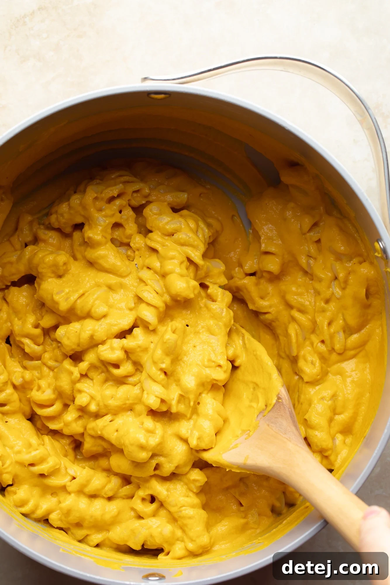 A beautifully plated bowl of vegan pumpkin mac and cheese, artfully garnished with a fresh sprig of thyme. The creamy orange pasta fills the bowl, exuding warmth and inviting indulgence, presented from an eye-level perspective.