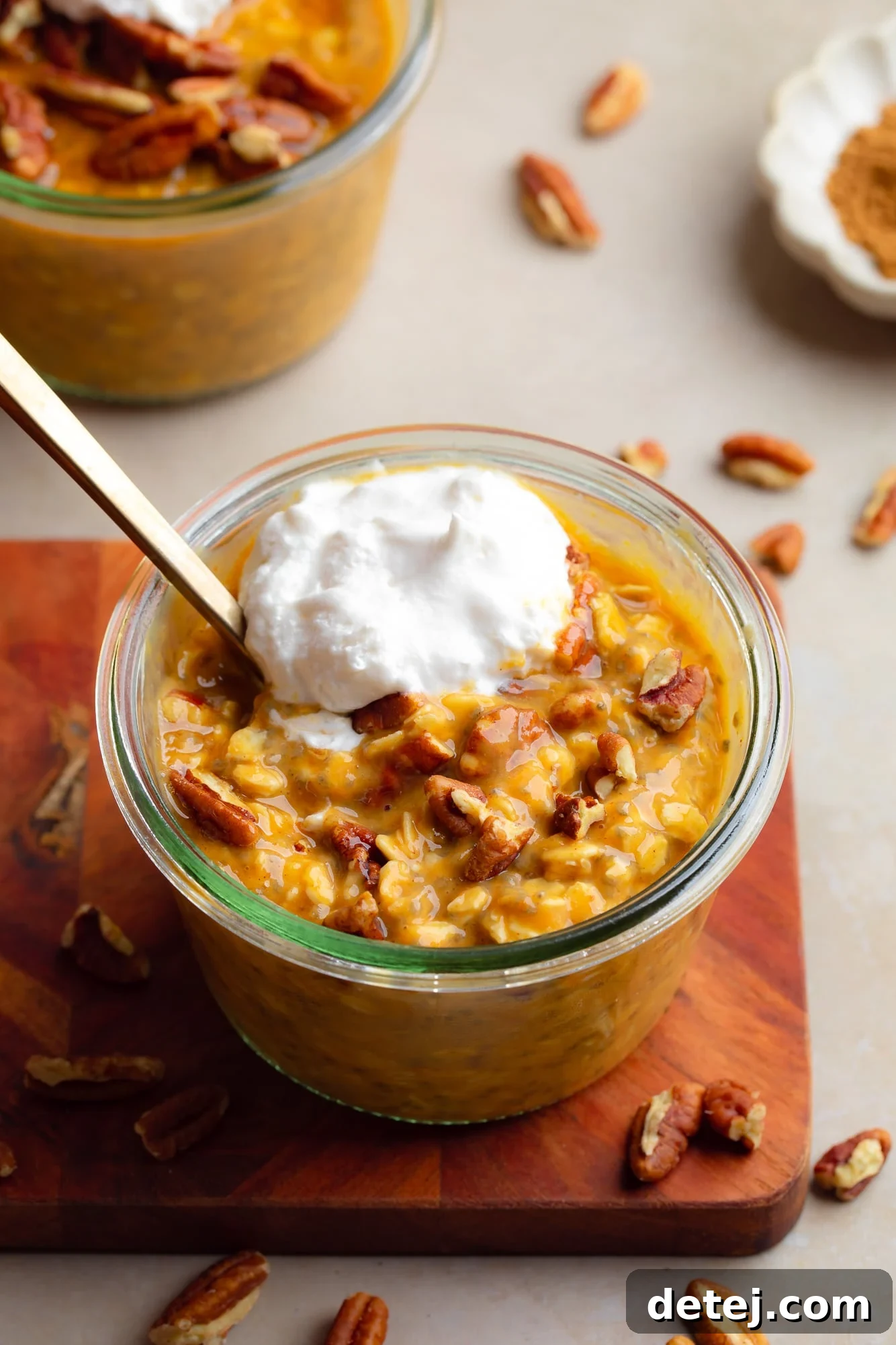 a glass jar of pumpkin overnight oats topped with pecans and whipped cream.