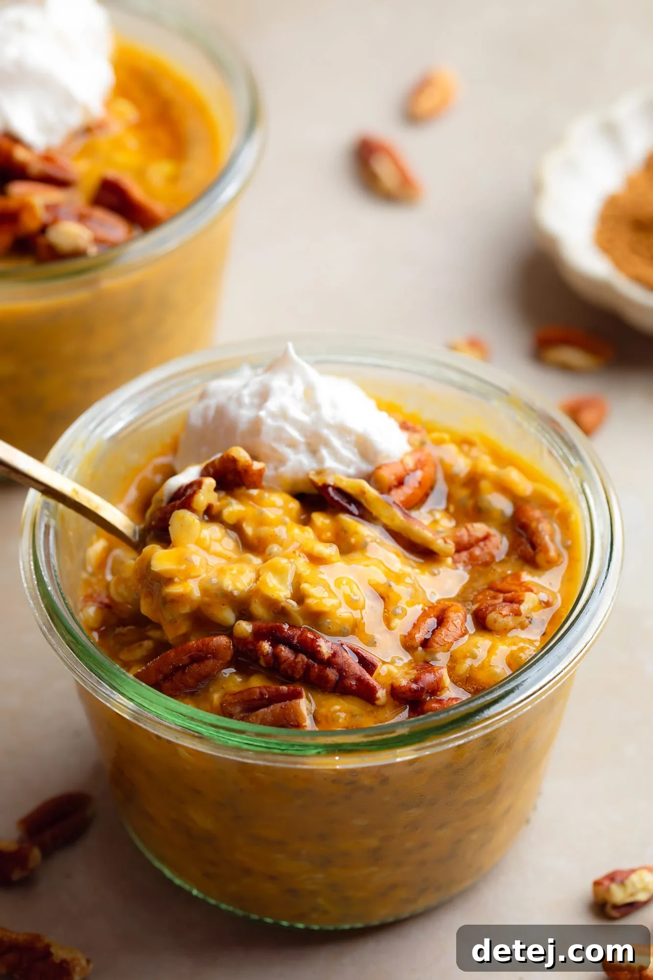 a glass jar of pumpkin overnight oats topped with pecans and whipped cream.