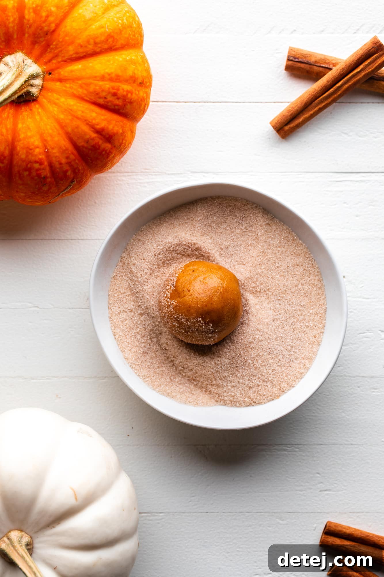 rolling a vegan pumpkin snickerdoodle cookie dough ball in a bowl of cinnamon sugar.