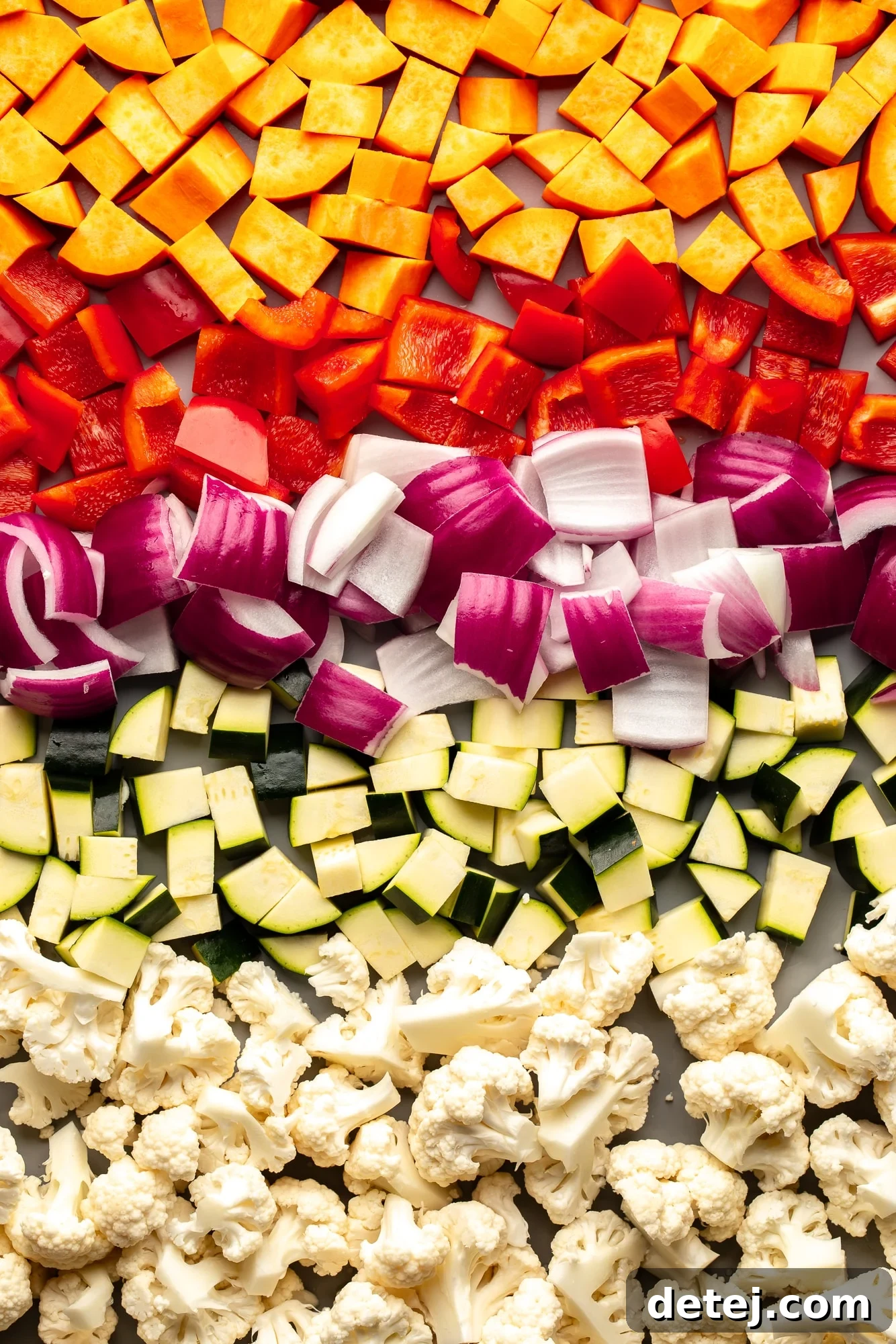 Overhead view of a medley of raw chopped vegetables, seasoned and ready for roasting on a sheet pan.