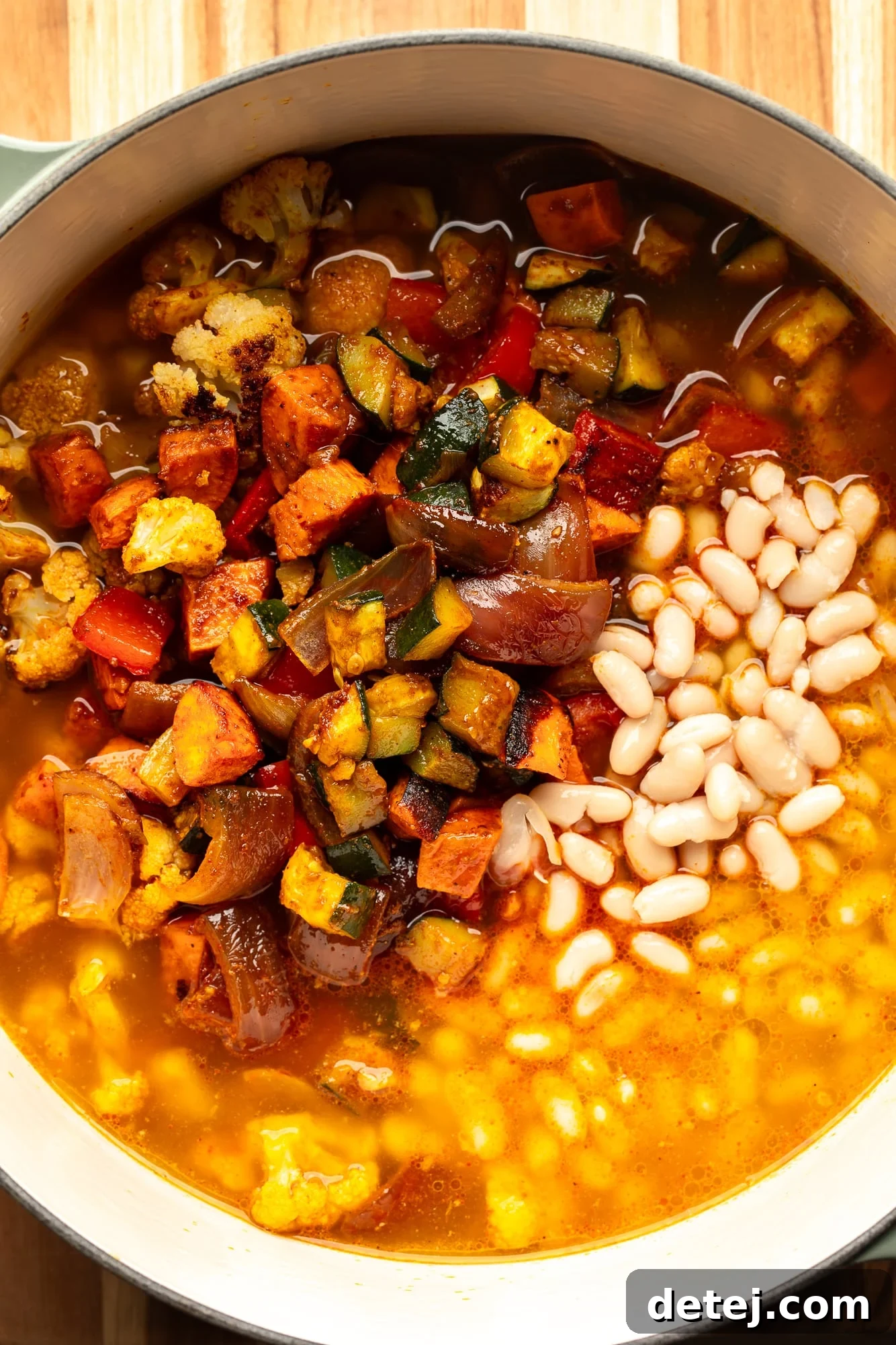 Overhead view of roasted vegetables, white beans, and broth simmering in a large pot, ready for blending.